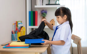 Young student in uniform packing books into school bag.