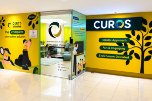 Bright yellow CUROS learning center booth in a mall, featuring education-themed graphics, “Holistic Approach,” and “Fun & Engaging” messaging.