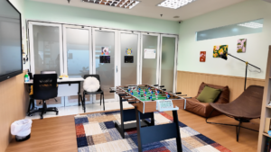 cozy room with Foosball table in the middle, couch and shelf filled with board games on the right.